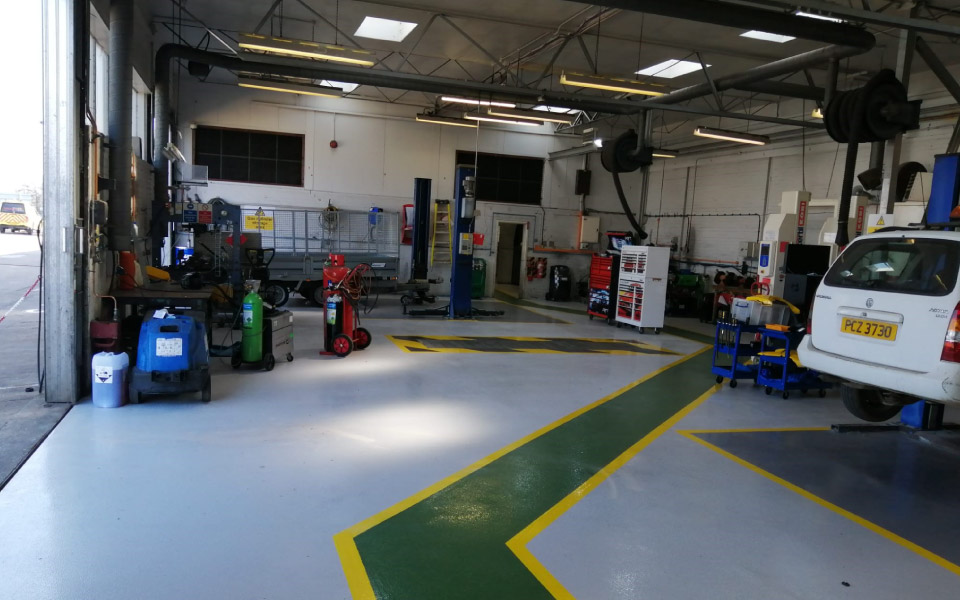 Anti-slip floor coating on coloured epoxy resin walkways guiding engineers through the vehicle workshop, designed and installed by CCS Garage Equipment