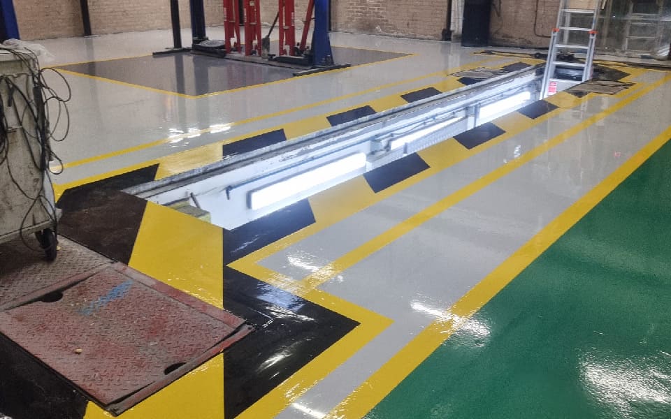 LED-lit commercial vehicle inspection pit, marked by long-lasting floor paint to indicate a potential fall hazard in the East Midlands Airport vehicle workshop